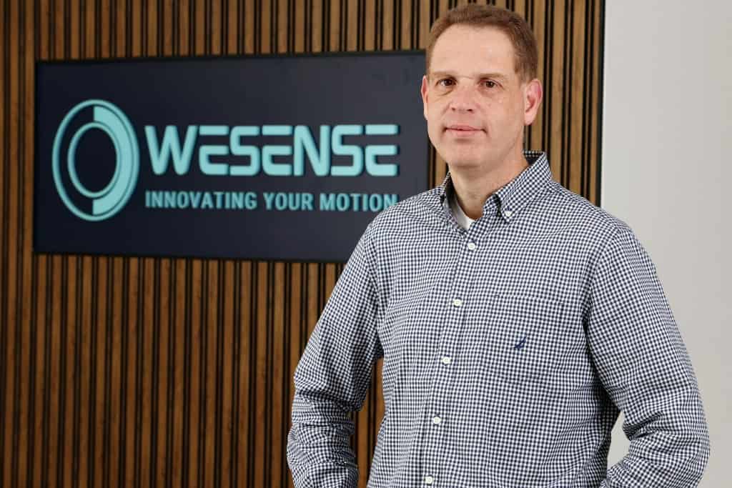 Professional portrait of WeSense team member in front of company logo.