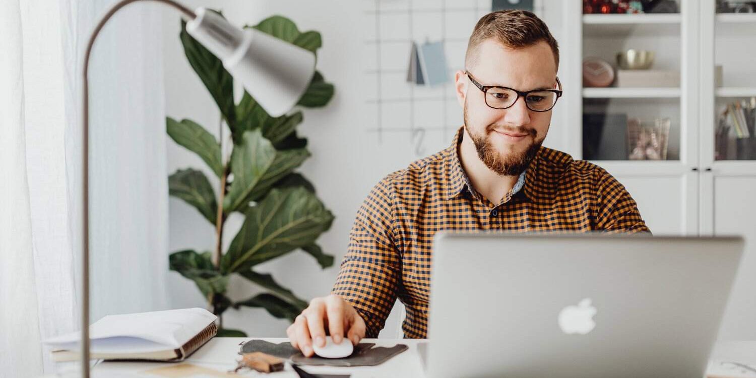 Man working on a laptop in a bright, organized home office setting.